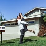 A joyful couple celebrating their new home purchase in front of a house with a sold sign.