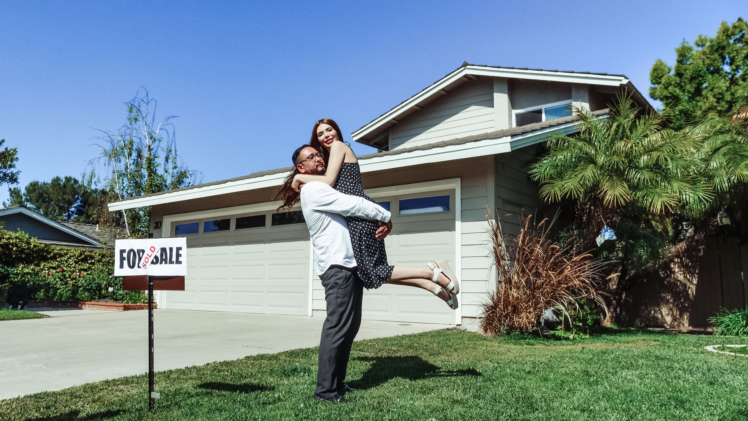 A joyful couple celebrating their new home purchase in front of a house with a sold sign.
