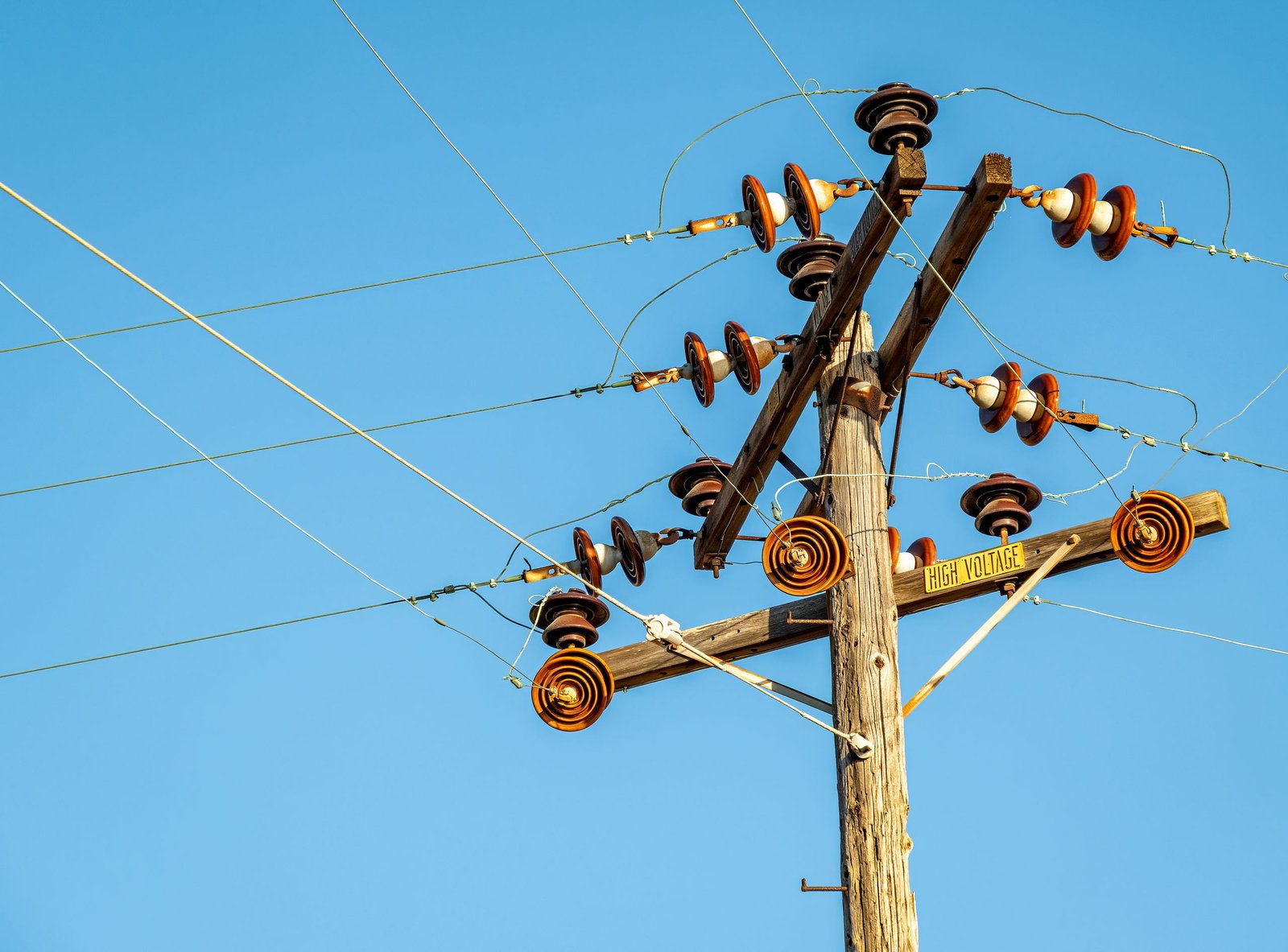 High voltage power line and insulators captured against a clear blue sky.