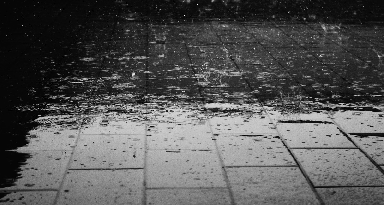 Monochrome image of raindrops creating splashes on a wet paved surface. How does winter affect solar system performance and will my electric bill go up?